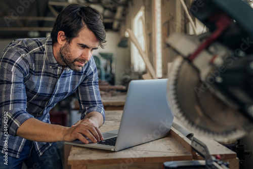 Carpenter working on a laptop in his woodworking studio photo