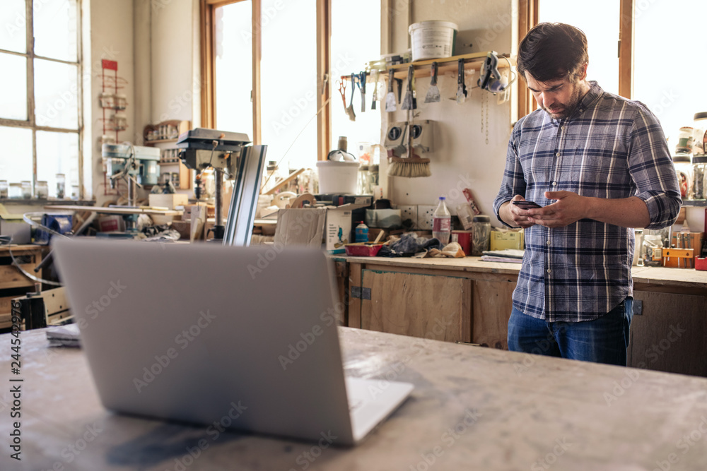 Woodworker reading a cellphone text while working in his studio