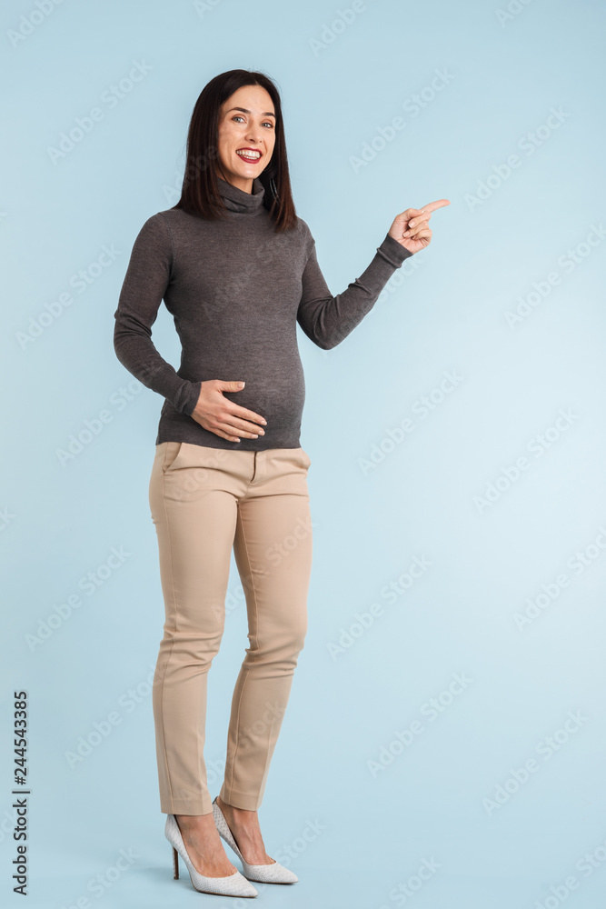 Pregnant woman isolated over blue wall background pointing to copyspace. Pregnant woman isolated over blue wall background pointing to copyspace.