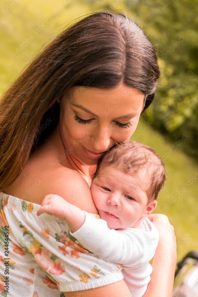 A beautiful young mother standing next to a stroller in the park and holding her baby girl in her arms on a sunny day. A beautiful young mother standing next to a stroller in the park and holding her baby girl in her arms on a sunny day.