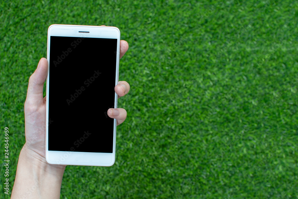 hand holding smartphone on green grass background