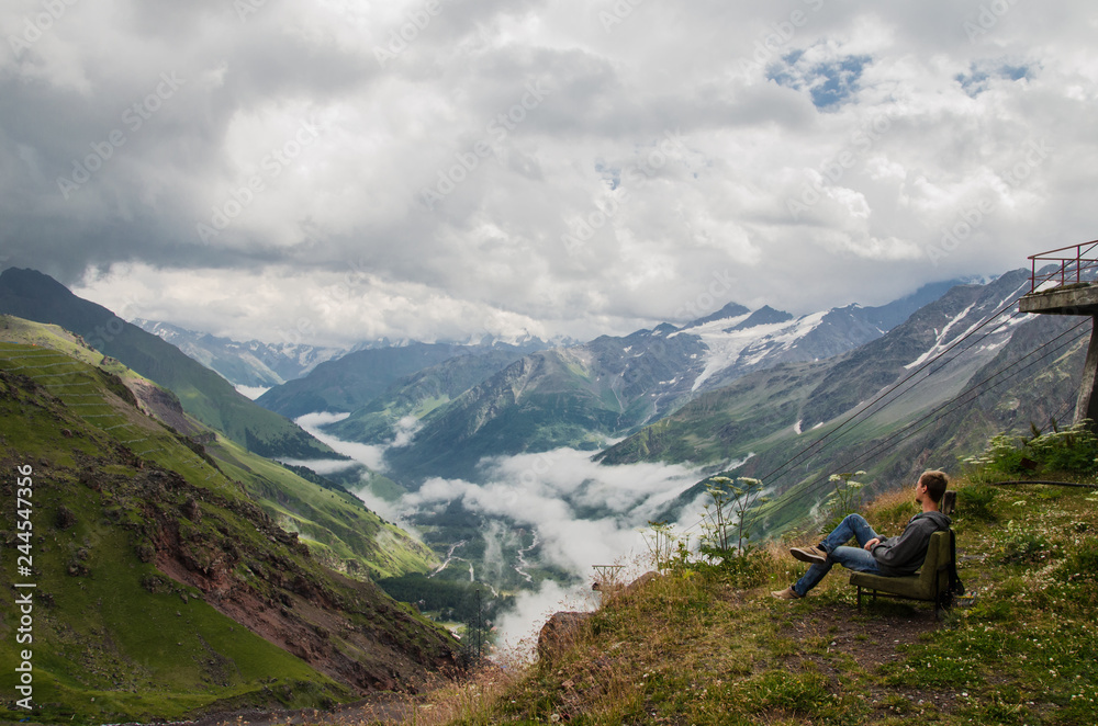 young man sitting on a chair on the grass in the mountains. Mountain gorge
