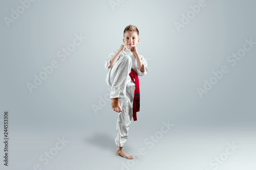 Creative background, a child in a white kimono makes a kick, on a light background. The concept of martial arts, karate, sports since childhood, discipline, first place, victory. copy space.