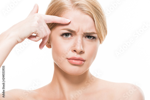 unhappy young woman pointing at wrinkles on forehead and looking at camera isolated on white