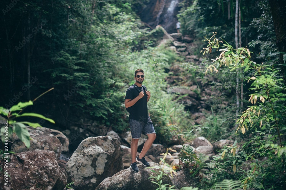 Fototapeta premium Handsome guy on the rocks at a tropical waterfall.