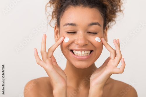 Laughing girl applying moisturizing cream on her face