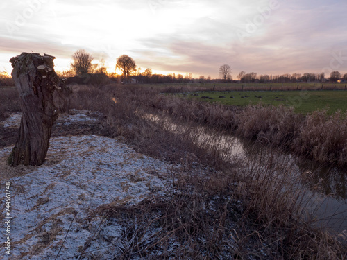 Abendstimmung an einem Bach im Norden von Deutschland. An Ufer liegt etwas Schnee und das trockene Gras spiegelt sich im Wasser. photo