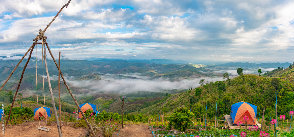 Panorama view of the mountain valley with tourists tent on the foreground and cloudy sky with mist in the background.