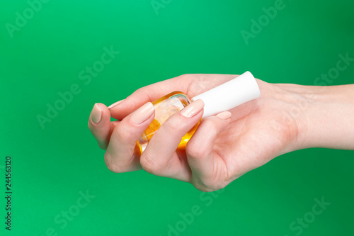Female's hand holding bottle with yellow nail polish of green background. 