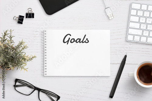 Creating goals list on notepad on office desk surrounded with office supplies. White wooden work desk. photo