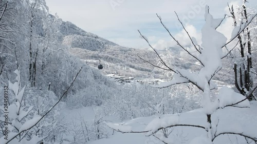 Aerial view over snowy mountain ridge valley with clouds, cable car lifting. Outdoor snow alpine wild nature tourist gondola transportation in winter. High altitude gondola in winter. Ski Gondola