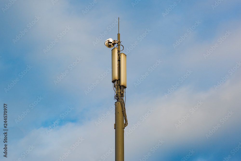 A pole with cellular repeaters against a blue cloudy sky