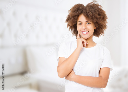 Smiling young african american woman with perfect skin care and healthy curly afro hair at home background. Blank t shirt and summer concept. Copy space