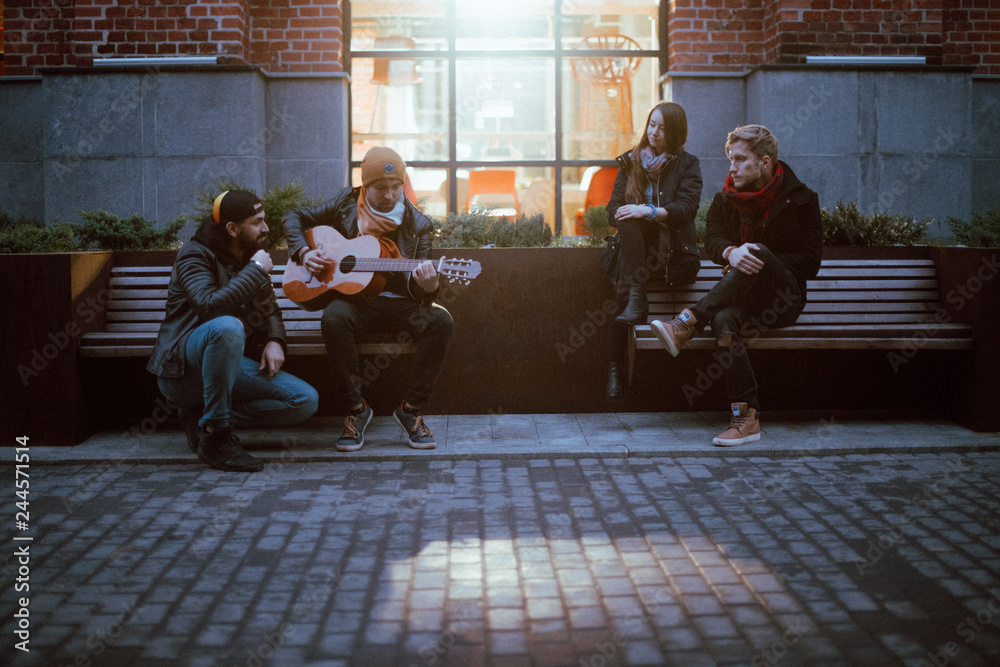 A company of friends on the bench plays the guitar.