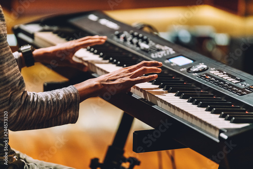 Man playing electronic musical keyboard synthesizer by hands on white and black keys in recording studio.