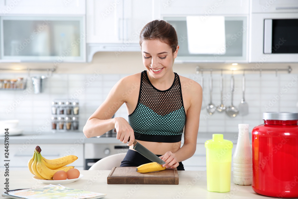 Young woman preparing protein shake at table in kitchen