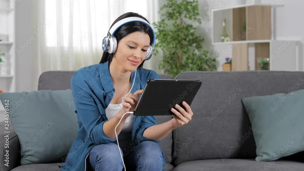 Happy woman selecting and watching media content on a tablet sitting on a couch at home Happy woman selecting and watching media content on a tablet sitting on a couch at home