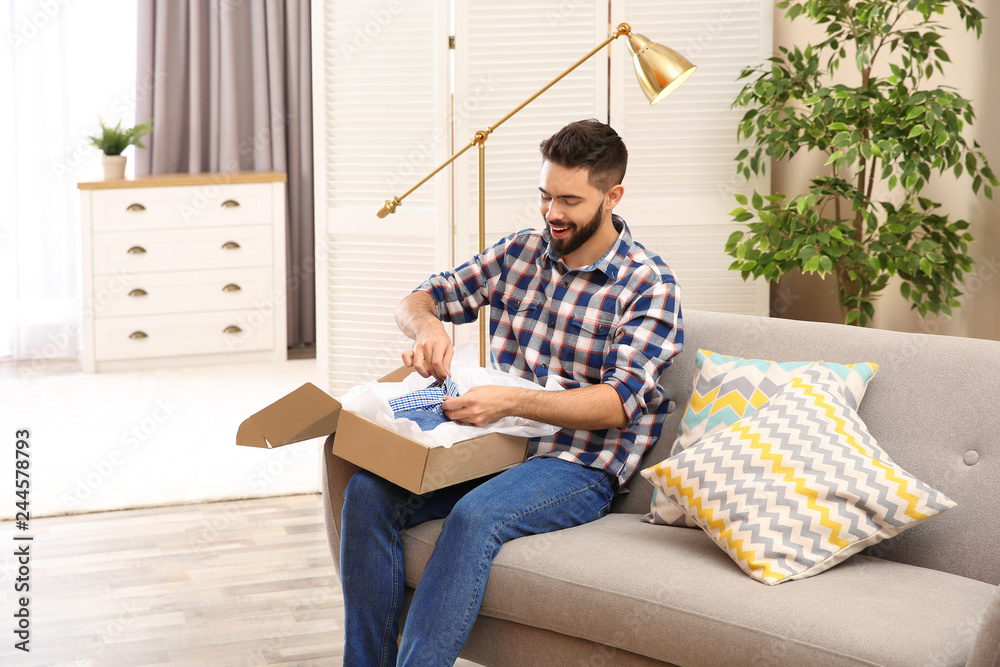 Fototapeta premium Young man opening parcel on sofa at home