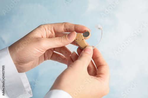 Woman putting battery into hearing aid on light background, closeup