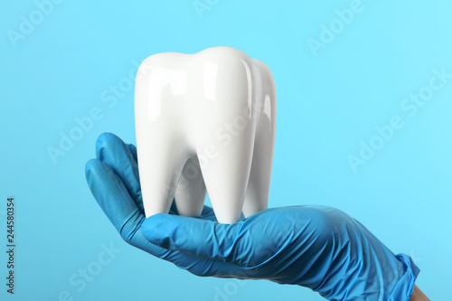 Fototapeta Naklejka Na Ścianę i Meble -  Dentist holding ceramic model of tooth on color background