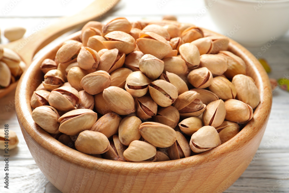 Organic pistachio nuts in bowl on wooden table, closeup Organic pistachio nuts in bowl on wooden table, closeup