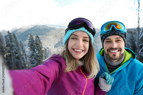 Happy couple taking selfie during winter vacation in mountains