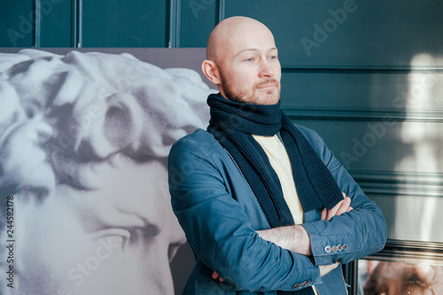 Portrait of attractive adult successful bald man art critic historian with beard in scarf in art gallery photo