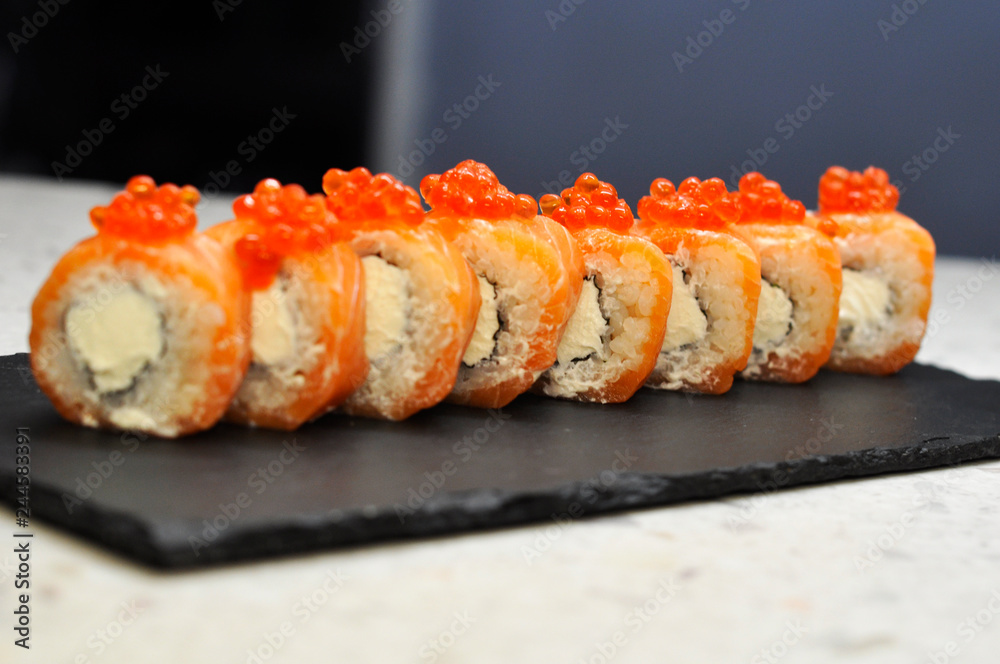 Eating Sushi with chopsticks. Sushi roll japanese food in restaurant. California Sushi roll set with salmon, vegetables, flying fish roe and caviar closeup. Japan restaurant menu