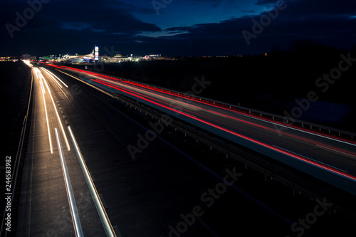 Motion blurred light tracks glowing to the darkness of highway traffic to the city just after sunset. Creative long time exposure photography.