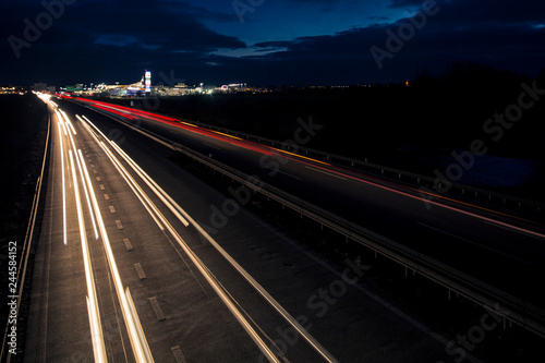 Motion blurred light tracks glowing to the darkness of highway traffic to the city just after sunset. Creative long time exposure photography.