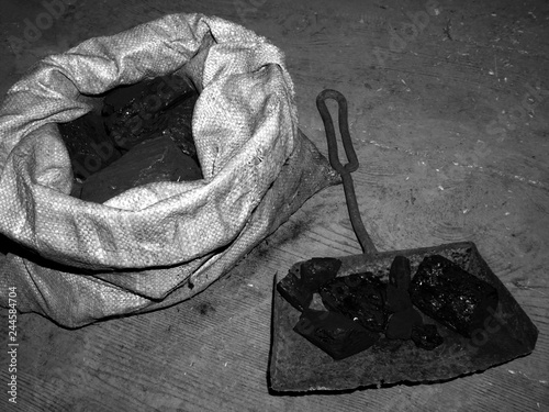 High contrast black and white photograph of coal in a sack and a shovel on dirty wooden floor photo