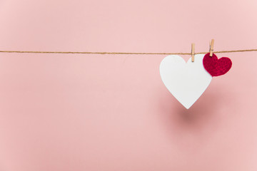 White and red love hearts pegged to a line against a pastel pink background