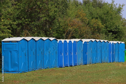 A many blue public WC toilets in a glade against the forest - tourists camping, infrastructure, summer tourist camp