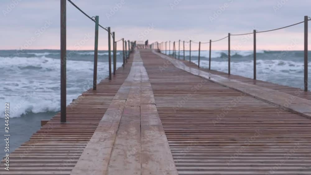 Waves splashes through the wooden pier in the sea. Family at the pier at sunset. Beautiful seascape. Waves splashes through the wooden pier in the sea. Family at the pier at sunset. Beautiful seascape.