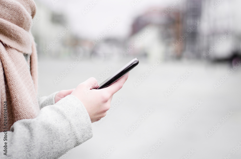 Closeup of young woman holding mobile phone in the street
