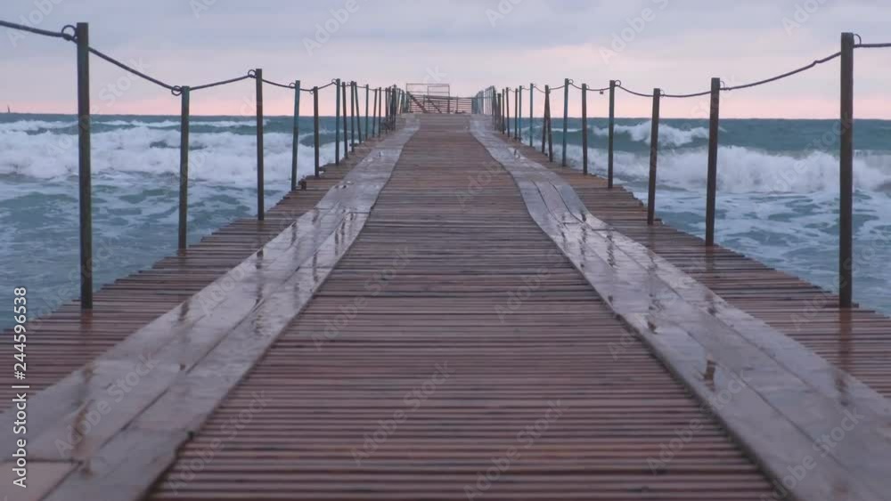 Waves splashes through the wooden pier in the sea. Beautiful seascape at sunset.