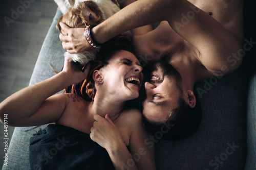 Young beautiful couple are lying on the couch and laughing. Dog sniffs them. selective focus. top view