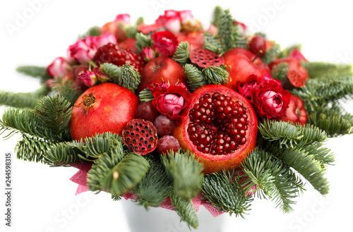 Huge edible fruit bouquet consisting of pomegranates, apples, grapes, rose flowers and fir twigs on white background. Close-up