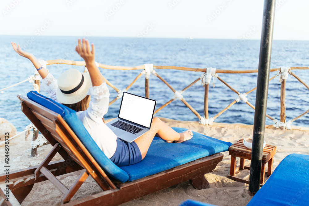 Young and beautiful woman with raised hands with the laptop relaxing on the beach