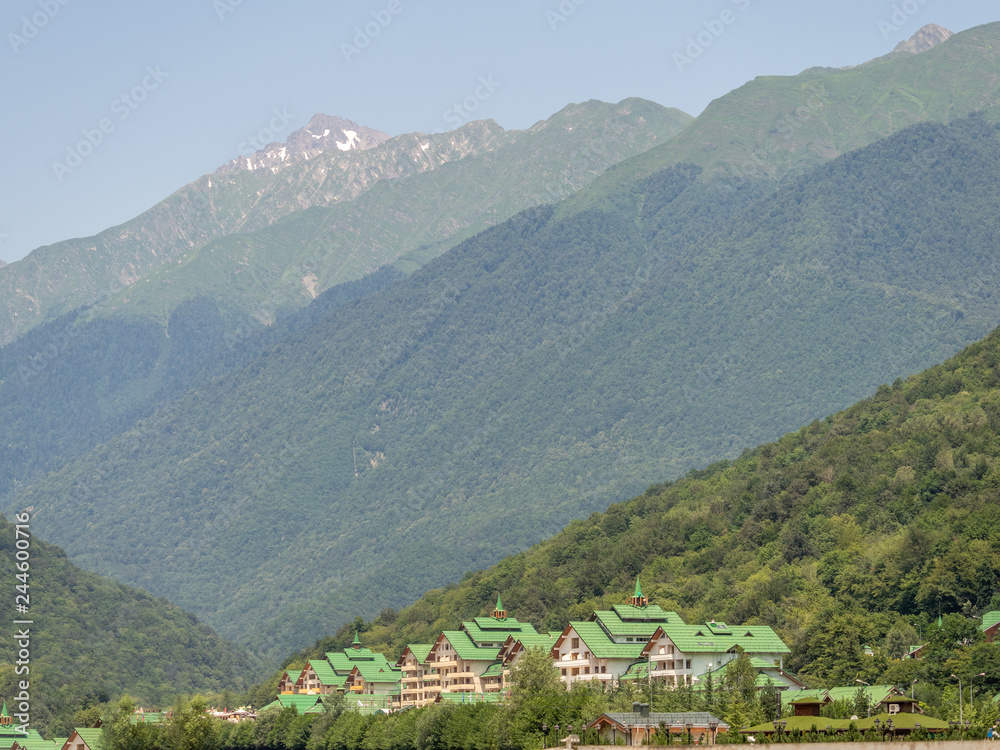 Hotel complex at the foot of high green mountains with snowy peaks