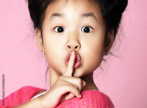 Asian kid girl in pink sweater shows shhh quiet sign on pink photo