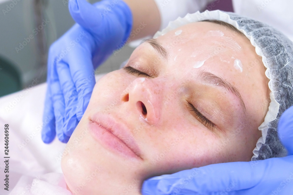 Beautician puts the cream on the woman's face. Cosmetologist facial treatment. Close-up.