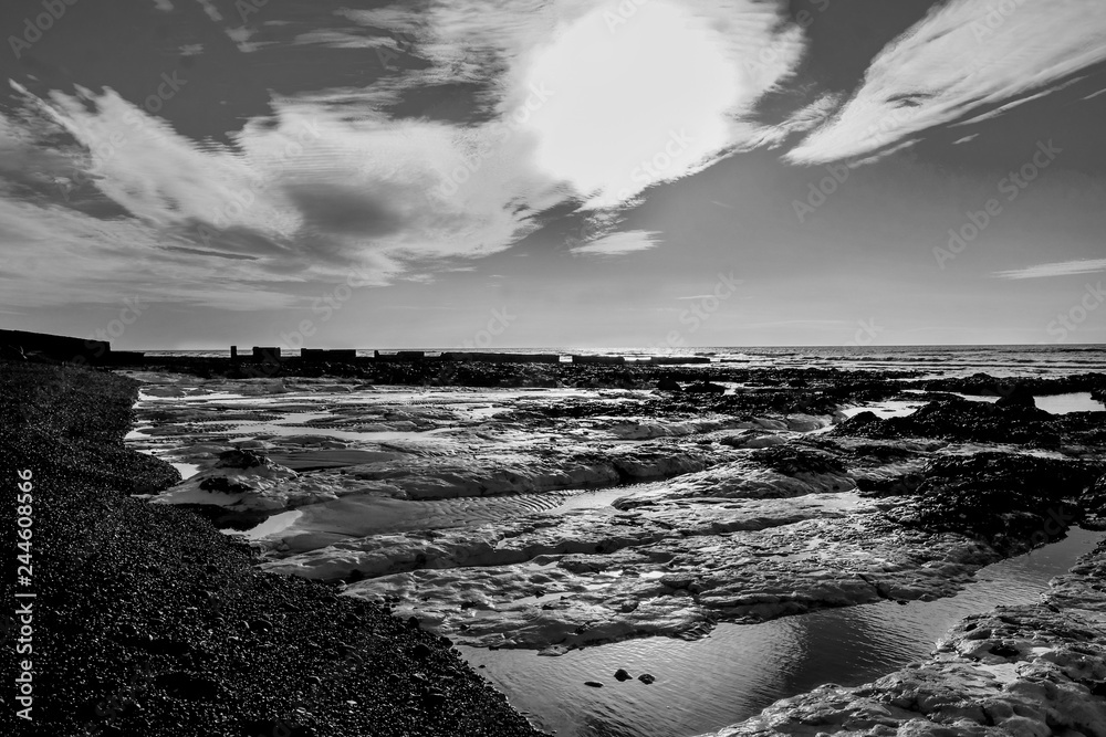 Rock pools on Ovingdean Beach in the winter, a pebble beach and sun in the sky, East Sussex, England,
