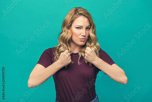 Girl straining muscles and shows fists. Attractive blonde posing on a blue background.