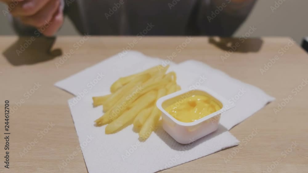 Woman is eating French fries with cheese sauce in cafe. Close-up hands. Woman is eating French fries with cheese sauce in cafe. Close-up hands.
