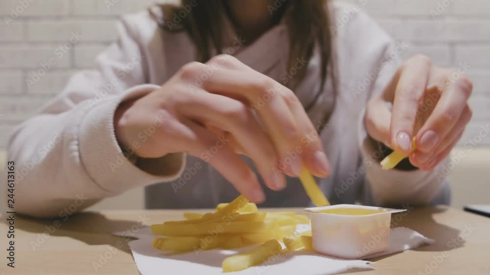Woman is eating French fries with cheese sauce in cafe. Close-up hands. Woman is eating French fries with cheese sauce in cafe. Close-up hands.