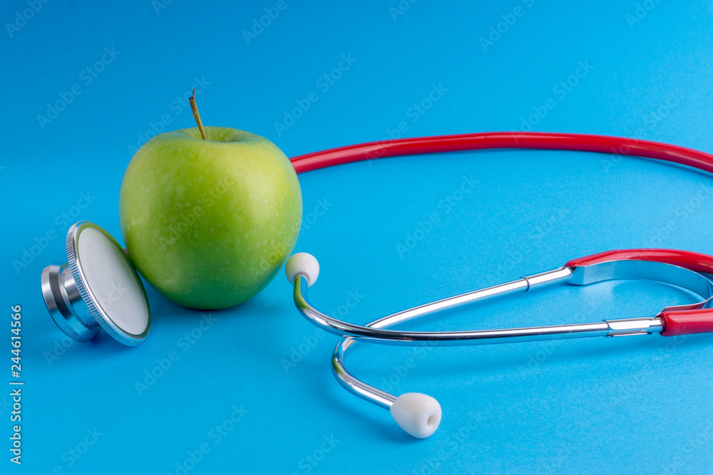 Green Apple with medical stethoscope isolated on blue background for healthy eating. Selective focus and crop fragment. Healthy, Diet and copy space concept Green Apple with medical stethoscope isolated on blue background for healthy eating. Selective focus and crop fragment. Healthy, Diet and copy space concept