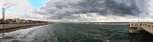 Fototapeta Naklejka Na Ścianę i Meble -  Panorama from the jetty to rough sea with scenic sky covered by clouds ready for the rain at distance a man alone looking the awesome seascape