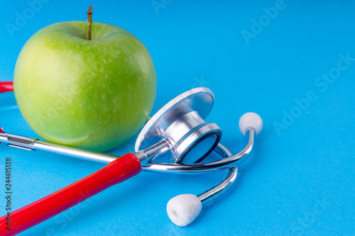 Green Apple with medical stethoscope isolated on blue background for healthy eating. Selective focus and crop fragment. Healthy, Diet and copy space concept photo