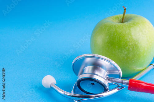 Green Apple with medical stethoscope isolated on blue background for healthy eating. Selective focus and crop fragment. Healthy, Diet and copy space concept photo